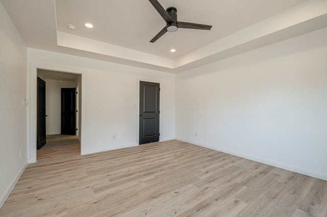 spare room with a raised ceiling, ceiling fan, and light hardwood / wood-style flooring