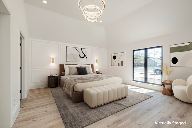 bedroom with an inviting chandelier, a towering ceiling, and light hardwood / wood-style flooring