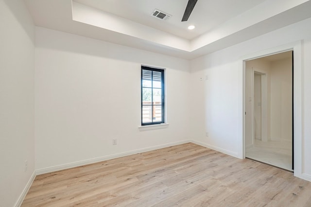 empty room featuring a tray ceiling, ceiling fan, and light wood-type flooring