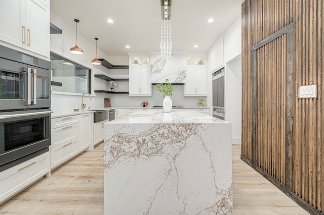 kitchen featuring a kitchen island, white cabinets, hanging light fixtures, light stone countertops, and stainless steel double oven