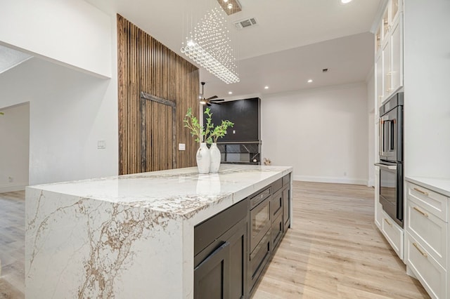 kitchen with light hardwood / wood-style flooring, a kitchen island, ceiling fan, light stone countertops, and white cabinets