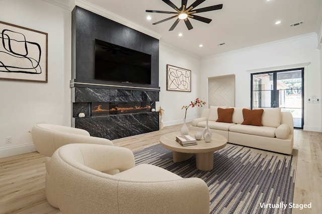 living room featuring hardwood / wood-style flooring, a premium fireplace, ceiling fan, and crown molding