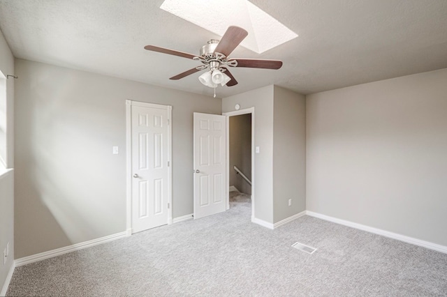 unfurnished bedroom featuring light carpet, a textured ceiling, a skylight, and baseboards