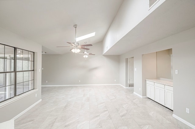 empty room with ceiling fan, vaulted ceiling with skylight, visible vents, and baseboards