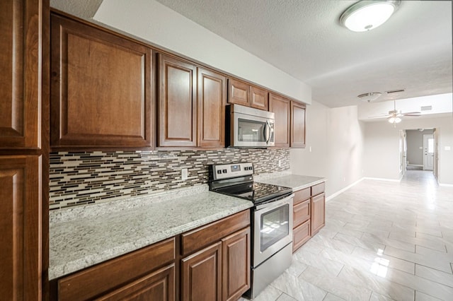 kitchen with brown cabinets, stainless steel appliances, tasteful backsplash, ceiling fan, and light stone countertops