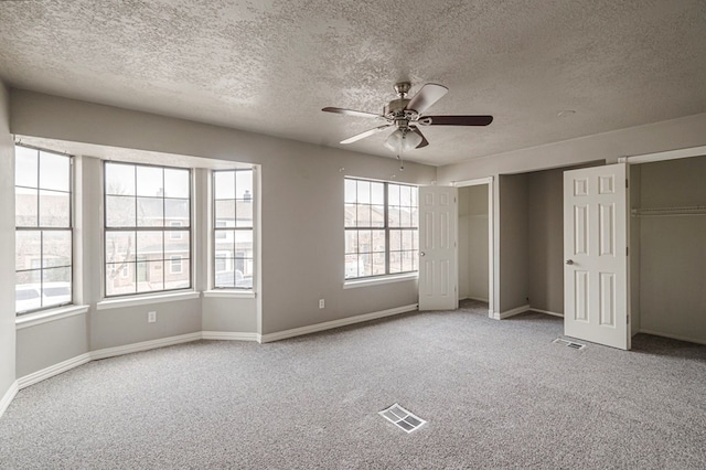 unfurnished bedroom with two closets, baseboards, visible vents, and carpet flooring