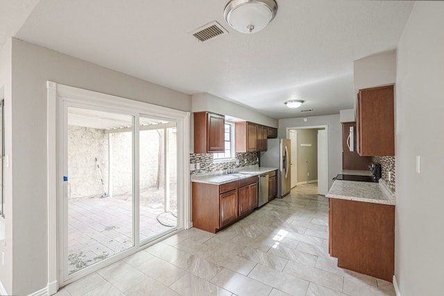 kitchen featuring tasteful backsplash, appliances with stainless steel finishes, brown cabinets, light countertops, and a sink