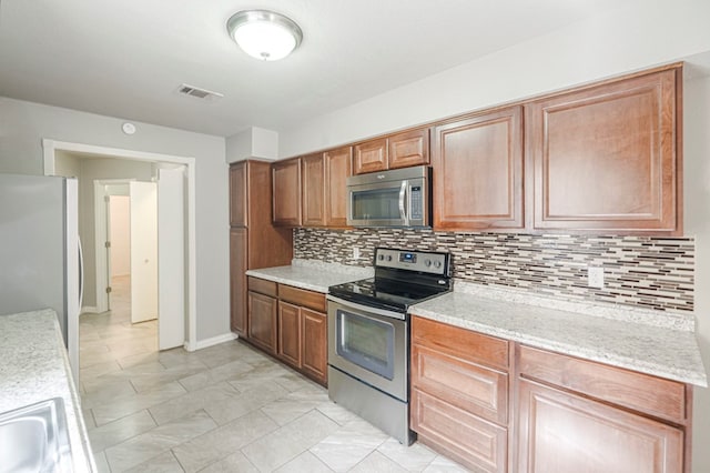 kitchen with light stone counters, stainless steel appliances, visible vents, backsplash, and brown cabinets