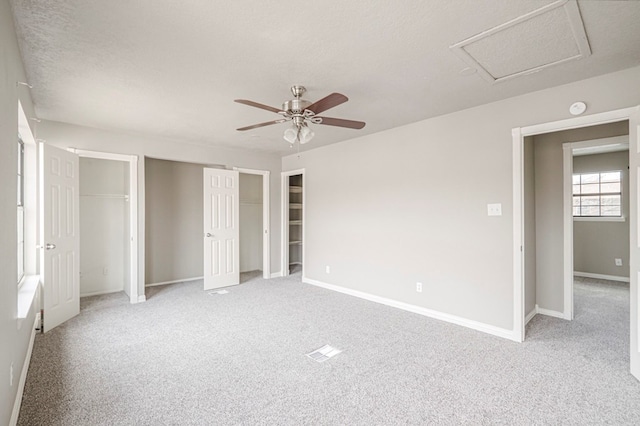 unfurnished bedroom featuring light carpet, a textured ceiling, two closets, and baseboards