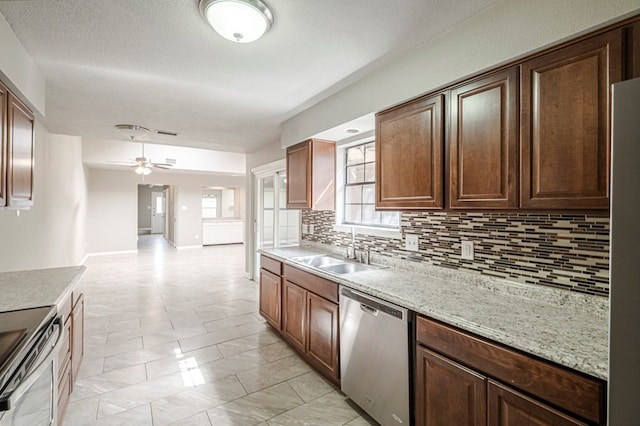 kitchen with ceiling fan, appliances with stainless steel finishes, a sink, light stone countertops, and backsplash