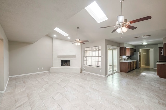 unfurnished living room featuring vaulted ceiling with skylight, baseboards, a ceiling fan, a fireplace, and a sink