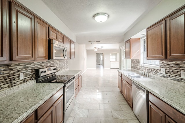 kitchen featuring stainless steel appliances, light stone counters, brown cabinetry, and a sink