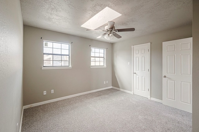 unfurnished bedroom with a skylight, carpet flooring, a textured ceiling, and baseboards