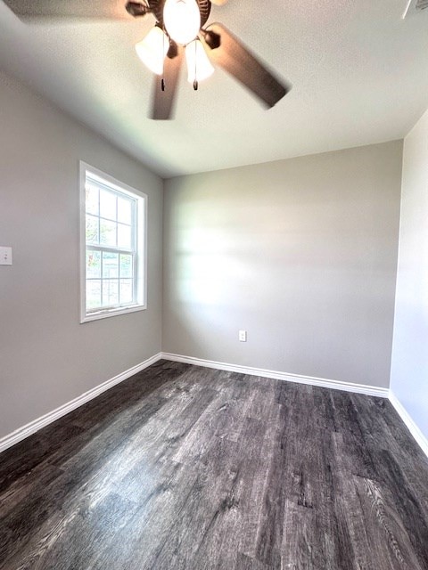 empty room featuring a ceiling fan, baseboards, and dark wood-style floors