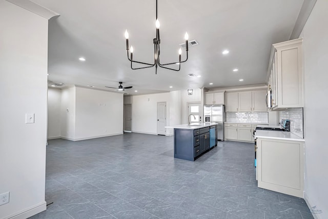 kitchen with ceiling fan with notable chandelier, sink, decorative backsplash, a kitchen island with sink, and stainless steel appliances