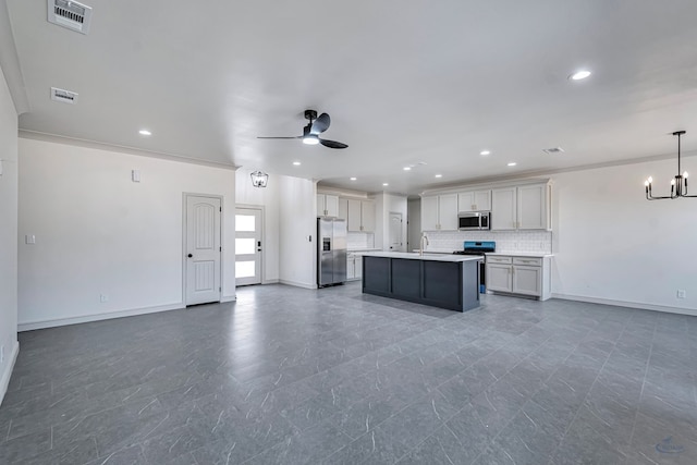 kitchen featuring appliances with stainless steel finishes, ceiling fan with notable chandelier, decorative backsplash, hanging light fixtures, and a center island with sink