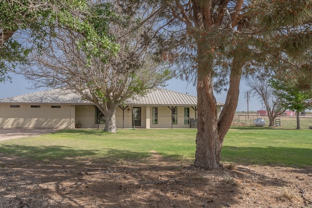 rear view of house featuring a lawn, fence, metal roof, and stucco siding