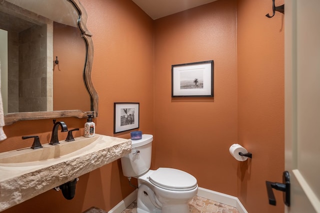 half bath featuring toilet, baseboards, and a sink