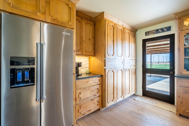 kitchen with dark countertops, light wood finished floors, brown cabinetry, tasteful backsplash, and high quality fridge