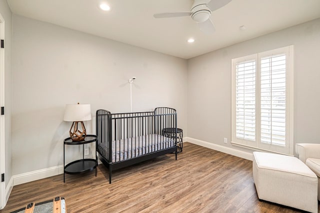 bedroom featuring wood-type flooring, a nursery area, and ceiling fan