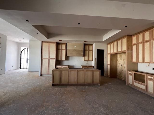 kitchen with glass insert cabinets, a tray ceiling, a kitchen island, and wall chimney range hood