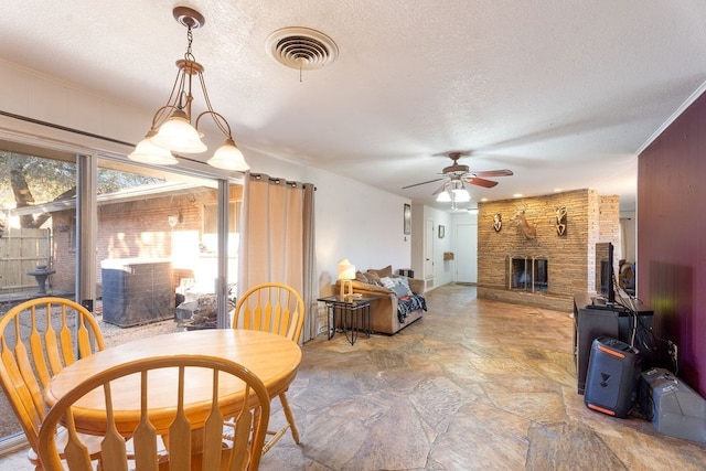 dining room with a stone fireplace, ceiling fan, and a textured ceiling