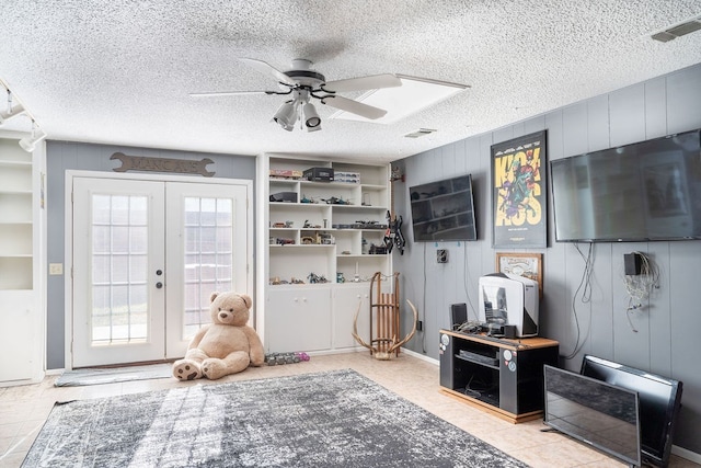 playroom featuring ceiling fan, a textured ceiling, wooden walls, and french doors