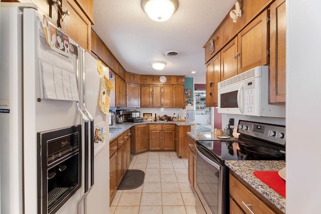 kitchen featuring a textured ceiling, light stone counters, light tile patterned flooring, and white appliances