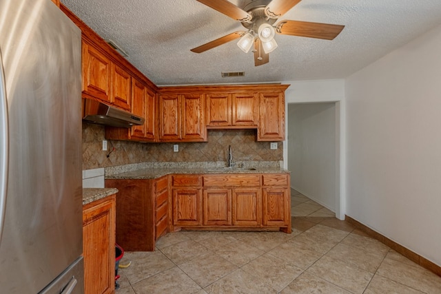 kitchen featuring stainless steel refrigerator, tasteful backsplash, sink, ceiling fan, and light stone countertops