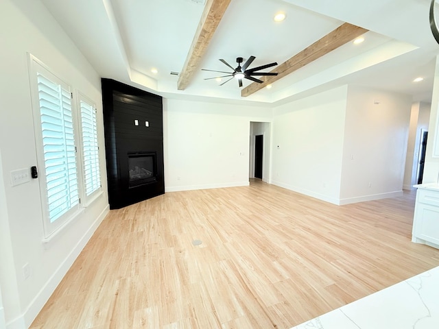 unfurnished room with a large fireplace, a raised ceiling, ceiling fan, light hardwood / wood-style flooring, and beamed ceiling