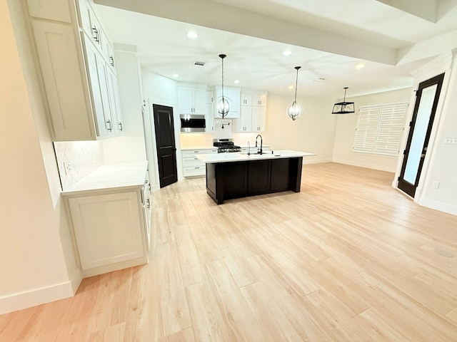 kitchen featuring a center island with sink, light hardwood / wood-style flooring, appliances with stainless steel finishes, decorative light fixtures, and white cabinetry