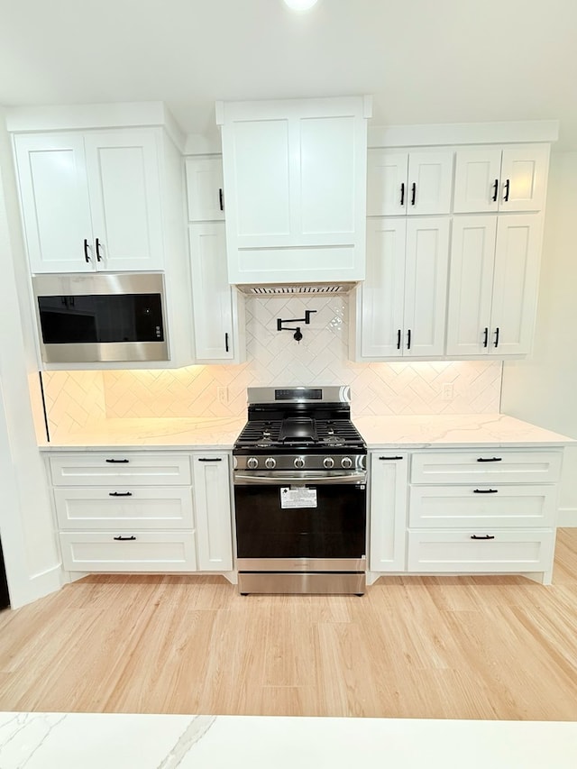 kitchen featuring stainless steel appliances, light stone counters, backsplash, white cabinets, and light wood-type flooring