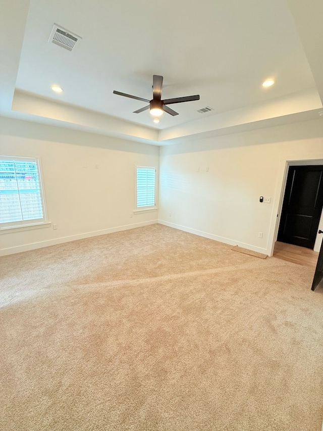 carpeted spare room with a raised ceiling and ceiling fan