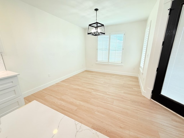 unfurnished dining area with light wood-type flooring and an inviting chandelier