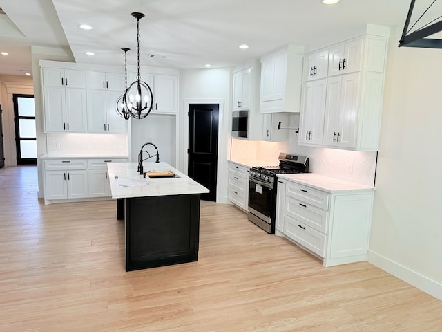 kitchen featuring white cabinetry, sink, stainless steel appliances, decorative light fixtures, and a kitchen island with sink