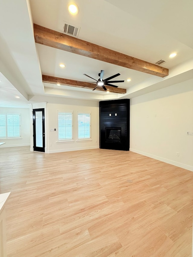 unfurnished living room featuring a large fireplace, light hardwood / wood-style floors, beam ceiling, and a wealth of natural light