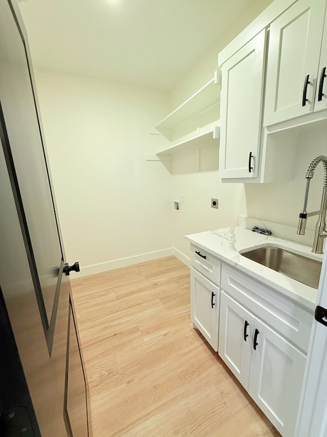 laundry area featuring electric dryer hookup, light hardwood / wood-style floors, cabinets, and sink