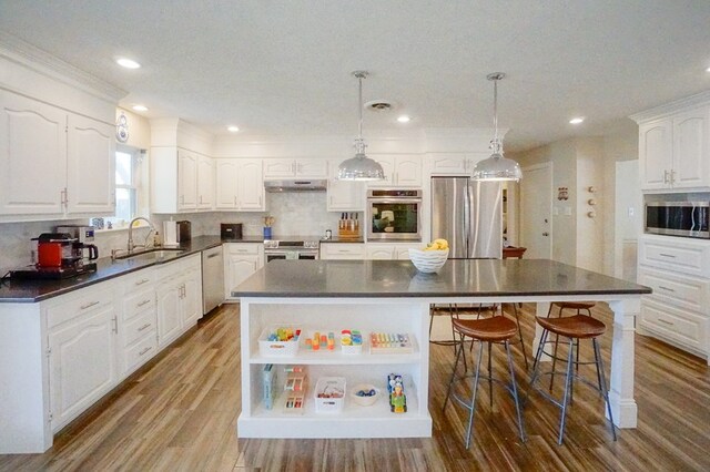 5 Bristol Ct, Midland, TX 79705 - kitchen with under cabinet range hood, dark countertops, a sink, appliances with stainless steel finishes, and white cabinetry
