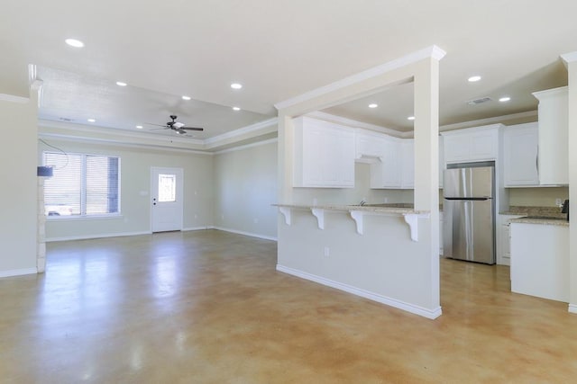 kitchen with white cabinetry, stainless steel fridge, a breakfast bar, and ornamental molding