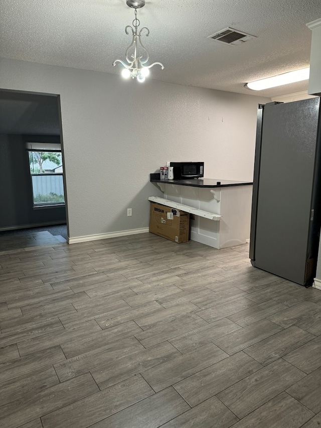 kitchen featuring stainless steel refrigerator, decorative light fixtures, a textured ceiling, and hardwood / wood-style flooring