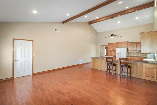 kitchen featuring a breakfast bar, beam ceiling, white fridge with ice dispenser, kitchen peninsula, and light wood-type flooring