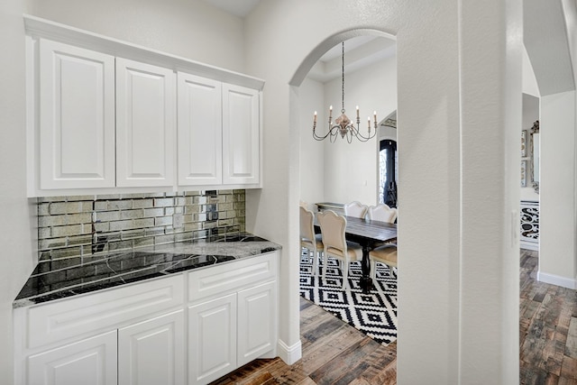 kitchen featuring backsplash, dark wood-style floors, dark stone counters, white cabinets, and a chandelier