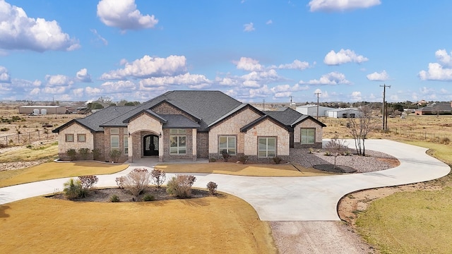 french country inspired facade with stone siding, curved driveway, brick siding, and a front lawn