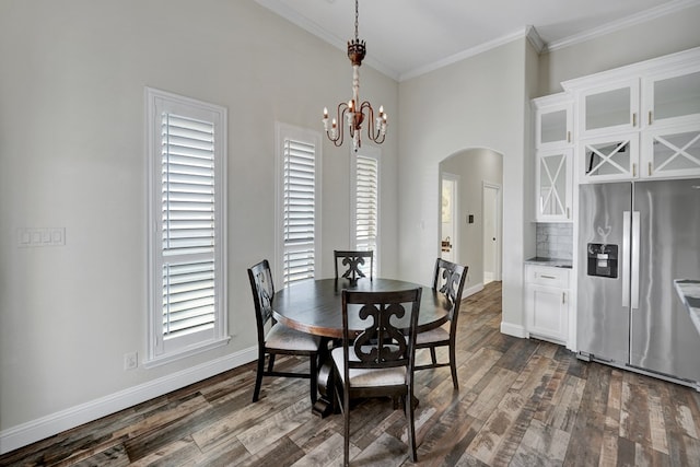 dining space with arched walkways, dark wood-type flooring, an inviting chandelier, and crown molding