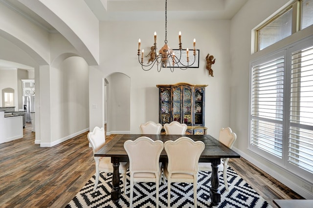 dining area featuring arched walkways, a notable chandelier, baseboards, and wood finished floors