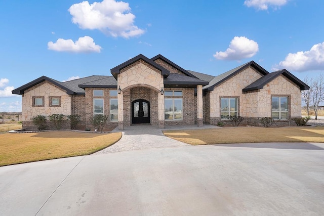 view of front facade featuring brick siding, a front lawn, french doors, and stone siding