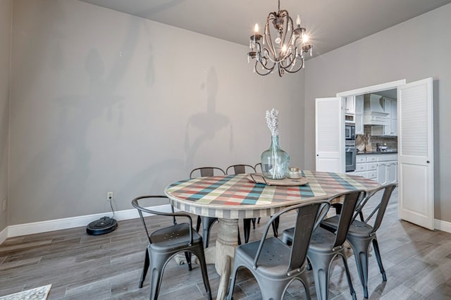 dining room with light wood-type flooring, a notable chandelier, and baseboards