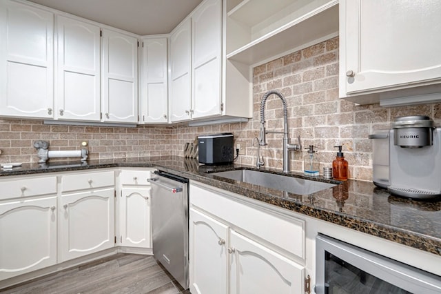 kitchen featuring dark stone countertops, stainless steel dishwasher, white cabinets, a sink, and wine cooler
