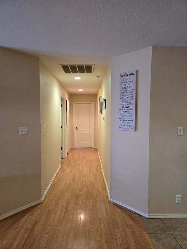 corridor with light wood-type flooring and a textured ceiling