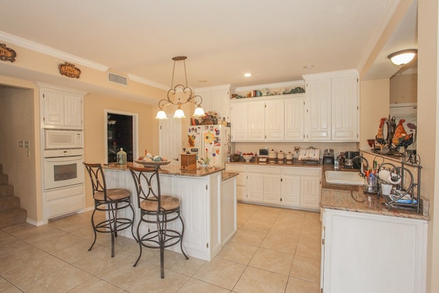 kitchen featuring stone counters, a center island, white cabinets, and white appliances